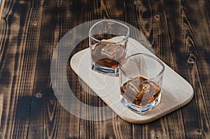 Two Glasses of cognac with ice cubes on a wooden table./ Two Glasses of cognac with ice cubes on a wooden background