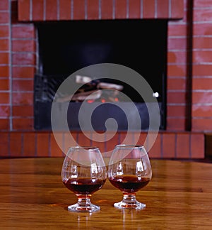 Two glasses of cognac on the old brick fireplace with bright fire