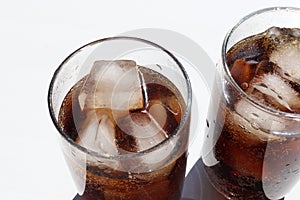 Two glasses of cola with ice cubes on white table. Top view, copy space. Hard light, shadow.  Refreshing summer drink