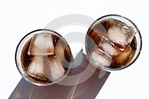 Two glasses of cola with ice cubes on white table. Top view, copy space. Hard light, shadow.  Refreshing summer drink