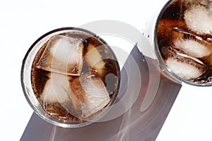 Two glasses of cola with ice cubes on white table. Top view, copy space. Hard light, shadow.  Refreshing summer drink