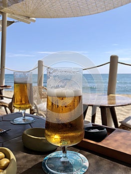 Two glasses of cold beer on a table in a beach bar in front of the Mediterranean Sea, in Malaga, Spain