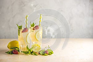 Two glasses of cold icy refreshing drink with lemon and strawberry served with bar tools on light pink table with white blooming