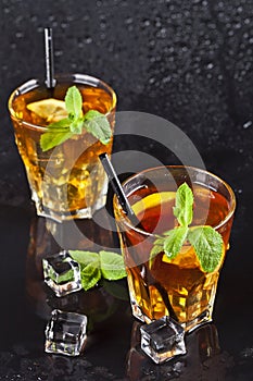 Two glasses with cold traditional iced tea with lemon, mint leaves and ice cubes