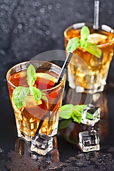 Two glasses with cold traditional iced tea with lemon, mint leaves and ice cubes