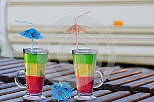 Two glasses with colorful cocktails and straws on a wooden lounger on the background Autocamper photo