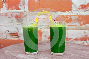 Two glasses with drinks from fresh greens, smoothies from green leaves saturated with chlorophyll against the background