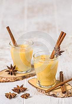 Two glasses of eggnogg with cinnamon sticks on white wooden background