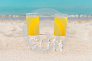 Two glasses filled with juice on sandy beach, against the background of the sea