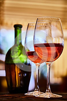 Two glasses filled with red wine and bottle in background