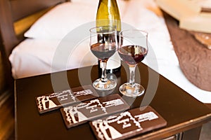 Two glasses are filled with red wine. Near the wineglasses stand a wine bottle and a few chocolates lying.