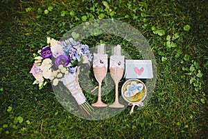 Two glasses with flowers, bottle of champagne and wedding rings on the grass. Wedding accessories