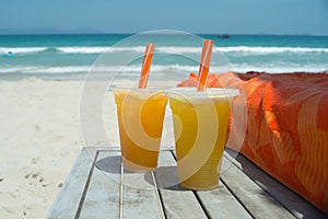 Two glasses of fresh orange juice on white sandy beach in front of sea