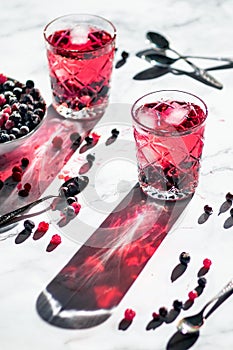 Two glasses full of bright fresh drink with red and black frozen currant in backlight