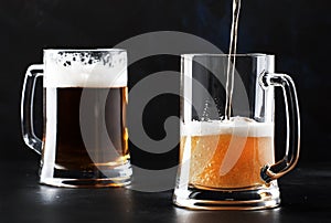 Two glasses of german light beer, beer poured into mug, dark bar counter, selective focus