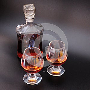 Two glasses and a glass bottle with cognac stands on a black background