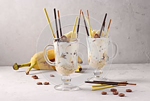 Two glasses of granola with chocolate and banana, decorated with sticks Pocky on gray background