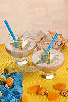 Two glasses with graped walnuts and slices of banana, green leaves of mint, physalis on a colorful background.