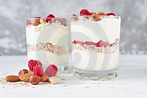 Two glasses of greek yogurt granola with raspberries, oatmeal flakes and nuts on a white background. Healthy nutrition