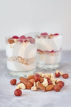 Two glasses of greek yogurt granola with raspberries, oatmeal flakes and nuts on a white background. Healthy nutrition