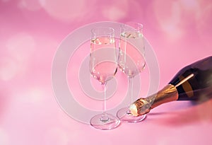 Two glasses of Ñhampagne and bottle of champagne on pink background