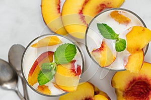 Two glasses of healthy fruit yogurt with fresh peaches, spoons and mint on white marble table. healthy breakfast
