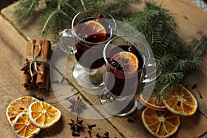 Two glasses of hot mulled wine with spices and sliced orange on wooden background. Close up