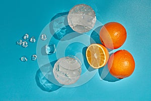 Two glasses with ice and oranges on blue background with shadow. Top view. Cocktail. Fresh orange juice