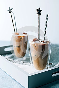 Two glasses of iced cappuccino coffee with ice on grey napkins on wooden tray. Cold brew with milk.