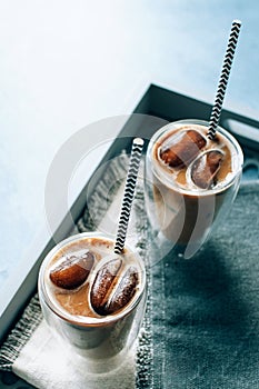 Two glasses of iced cappuccino coffee with ice on grey napkins on wooden tray. Cold brew with milk.