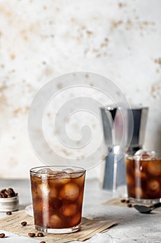 Two glasses of iced cold brew coffee with coffee beans on light table