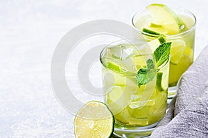 Two glasses of iced green matcha tea with lime, ice, fresh mint and grey napkin on light grey background