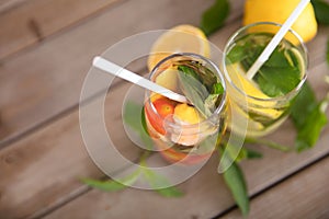 Two glasses of iced lemon mint tea and fresh lemon fruit and mint leaves next to the cup