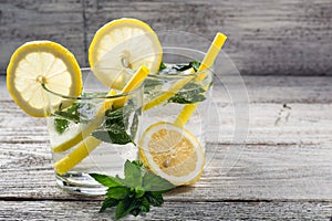 Two glasses of lemonade with lemon, mint and ice cubes on wooden background. Summer drink
