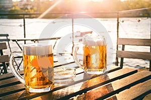 Two glasses of light beer with foam on a wooden table.On a boat. Garden party. Natural background. Alcohol. Draft beer. Landscape,