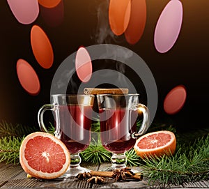 Two glasses with mulled wine against the background of fir branches and lights of garlands