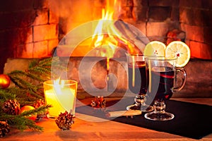 Two glasses with mulled wine, a candle, fir branches with decorations on a wooden table against the background of a