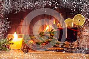 Two glasses with mulled wine, a candle, fir branches with decorations on a wooden table against the background of a