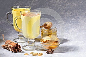 Two glasses for mulled wine with golden milk with ingredients on light grey background.