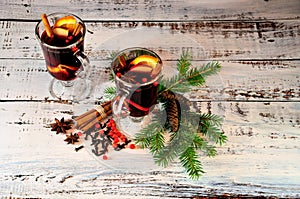 Two glasses of mulled wine with spices and fruit slices stand on a table surrounded by fir branches and cones