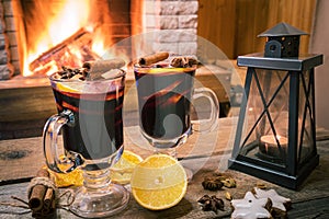 Two glasses of mulled wine on a wooden board before burning fireplace