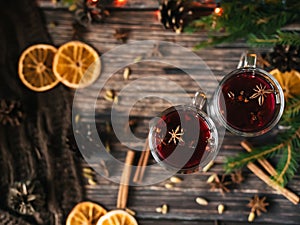 Two glasses with mulled wine on a wooden table with orange, cinnamon, cardamom, anise stars. Traditional winter hot