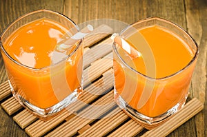 two glasses with orange juice with straws on a wooden support/two glasses with orange juice with straws on a wooden support. Top