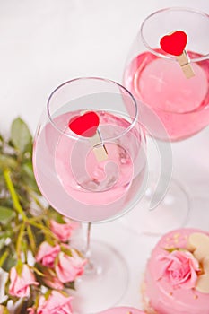 Two glasses with pink grape wine with clothpin heart shaped and roses on the background. Romantic dinner concept