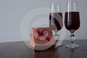 Two glasses with red liquid over a table and red gift box