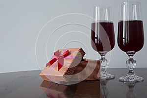 Two glasses with red liquid over a table and red gift box