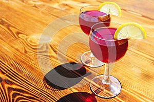 two glasses with red summer cocktails with lemon slices on a wooden background