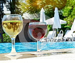 Two glasses of red and white wine are placed by the pool. The concept of a pleasant stay.