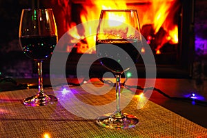 Two glasses of red wine against the background of a burning fireplace in hard reflective lighting. Romantic relaxed dinner by the