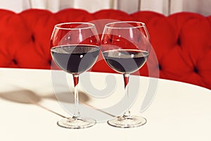 Two glasses of red wine, alcoholic drink, beverage, served on white table in cafe or bar on sofa background.